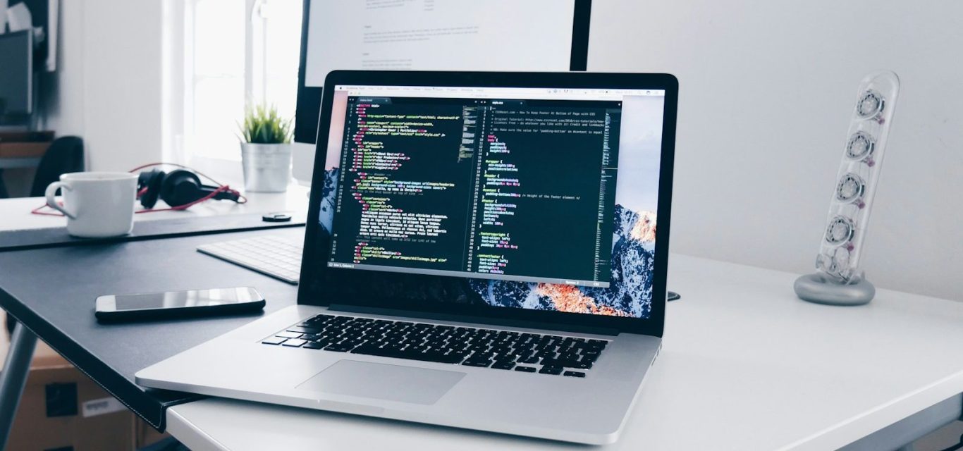 A MacBook with lines of code on its screen on a busy desk