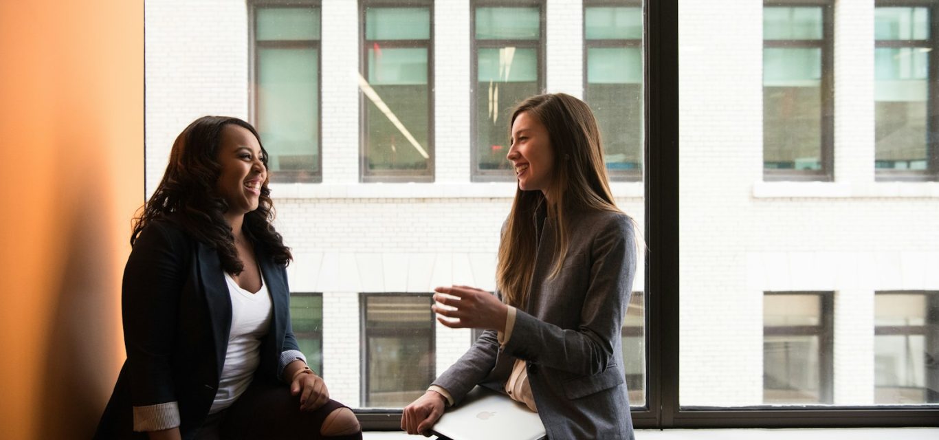 two woman sitting by the window laughing