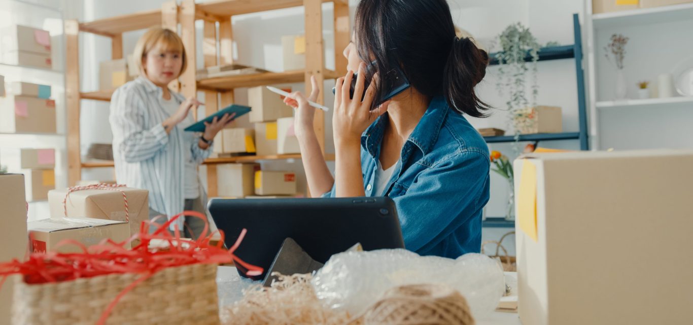 Young Asia businesswomen using mobile phone call receiving purchase order and check product on stock work at home office. Small business owner, online market delivery, lifestyle freelance concept.
